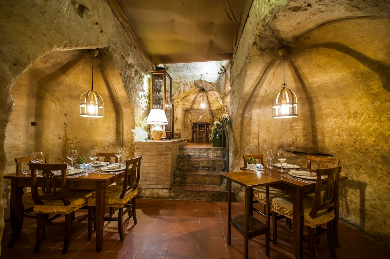 Sala scavata nel tufo dell'Antica Osteria da Divo a Siena, con archi, lampade in metallo e tavoli apparecchiati